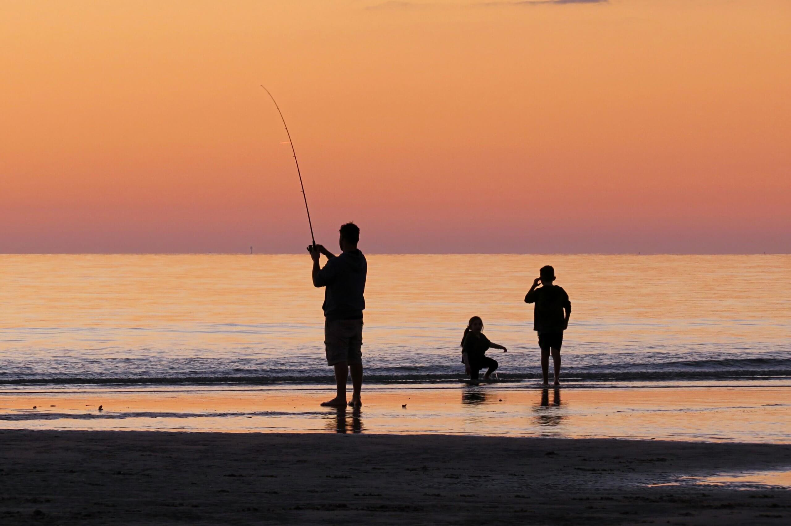 papa qui pêche avec ses enfants au bord de la mer au coucher du soleil