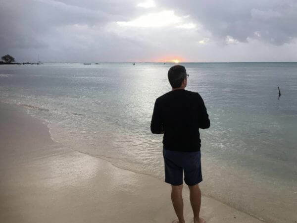 spot idéal pour la pêche. Pêcheur qui regarde l'horizon au coucher du soleil sur une plage de sable fin.